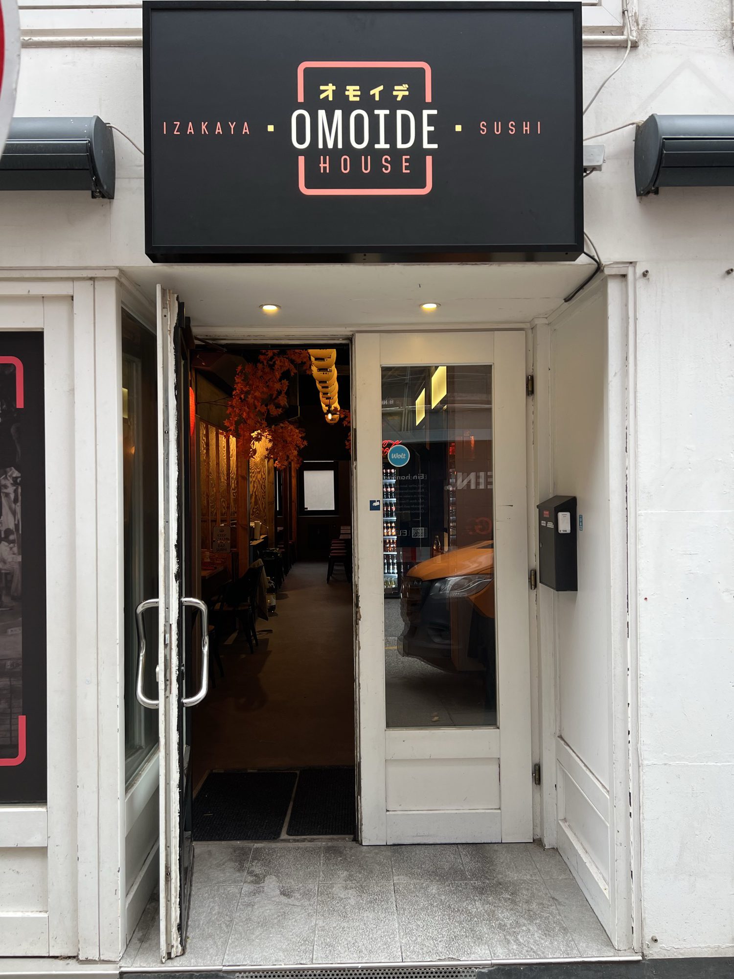 Der Eingang des OMOIDE HOUSE mit beleuchtetem Schild